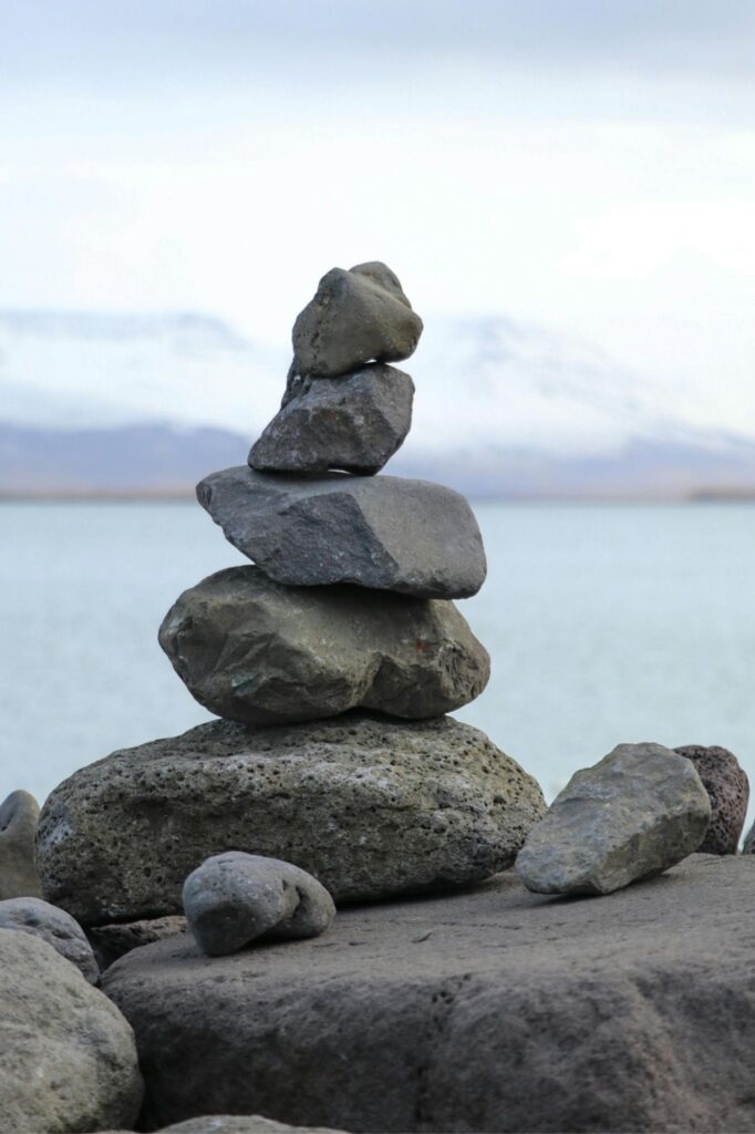Stacked rocks (cairn) balanced on a rocky shore with water and distant mountains in the background.