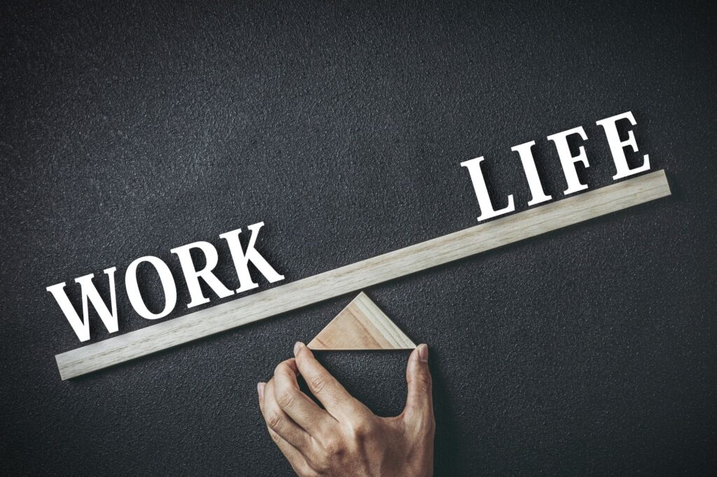 Words WORK and LIFE on wooden strips against a dark textured surface, with a hand adjusting the pieces, symbolizing work–life balance .