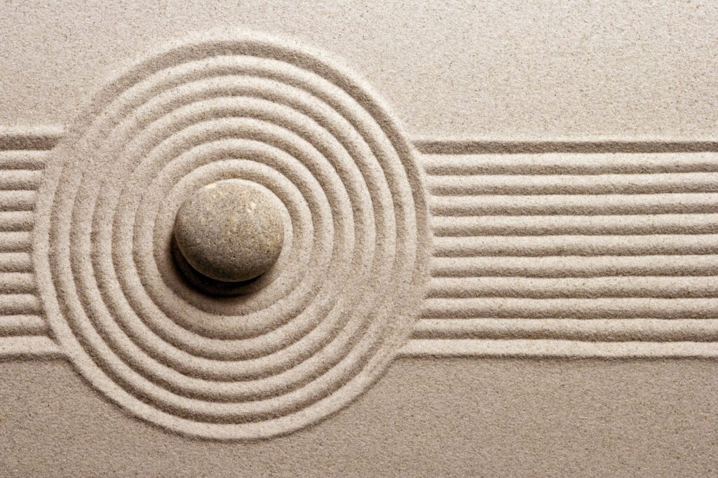 Stone in the center of circular sand grooves in a Zen garden, with straight lines to the side.