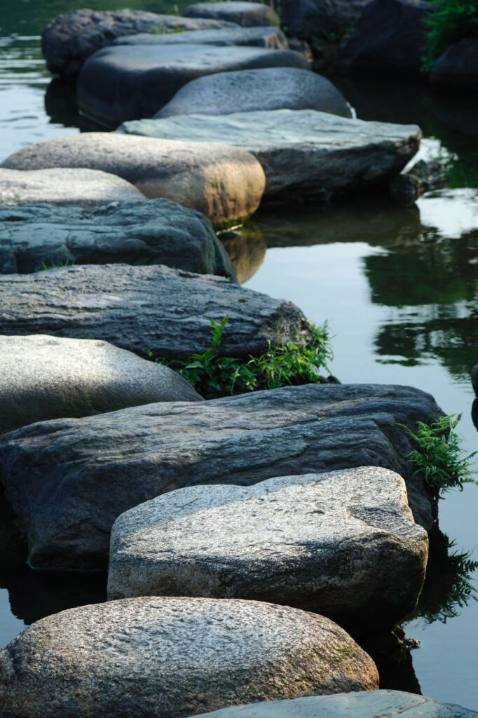 Smooth gray stones line a calm body of water, with reflections visible on the surface