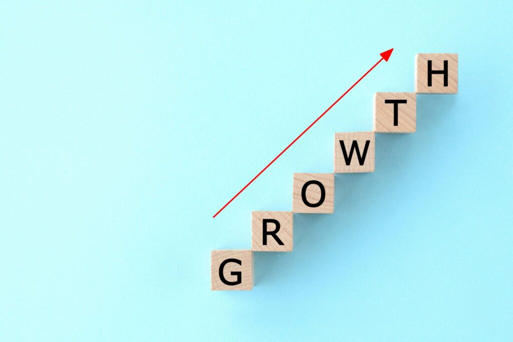 Wooden blocks arranged as steps spell out GROWTH with a red rising arrow alongside, signaling upward progress.