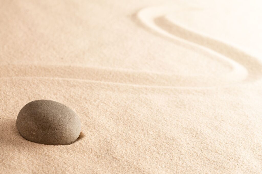 Two smooth brown pebbles resting on fine, sunlit sand at the beach.