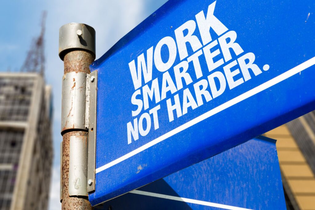 Blue sign reading 'WORK SMARTER NOT HARDER' in bold white letters on a blue background, mounted on a rusted metal pole nearby.