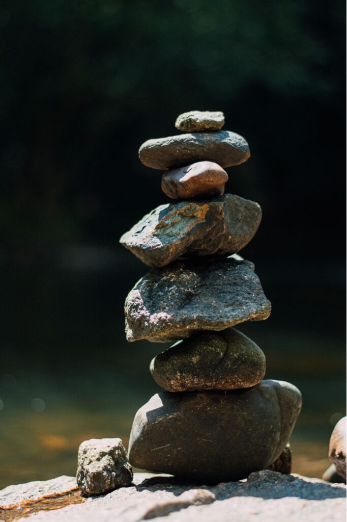 Stacked smooth rocks balanced into a vertical cairn on a sunlit rocky surface.