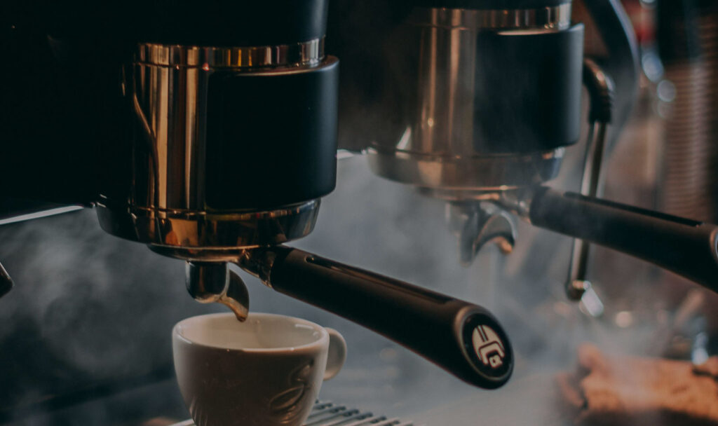 Espresso machine portafilter pouring into a small white cup with steam rising.