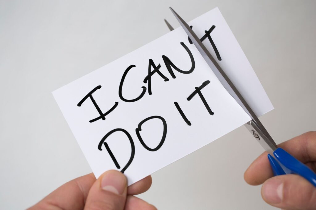 Close-up of hands using scissors to cut a white card that reads 'DO NOT' in bold black letters, on a light background.