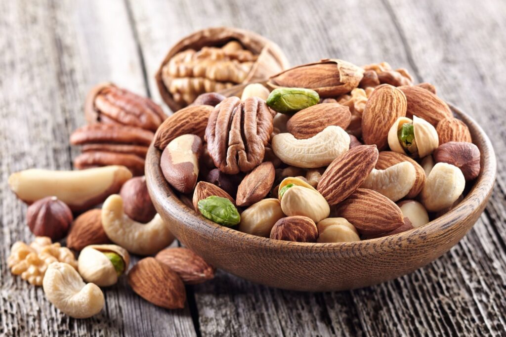 Assorted nuts in a wooden bowl on a rustic wooden table—almonds, pecans, pistachios, cashews and walnuts.