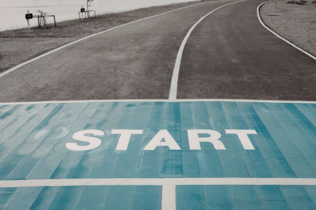 A race start line on a blue track with the word START visible, road curving into the distance by a lake on the left.