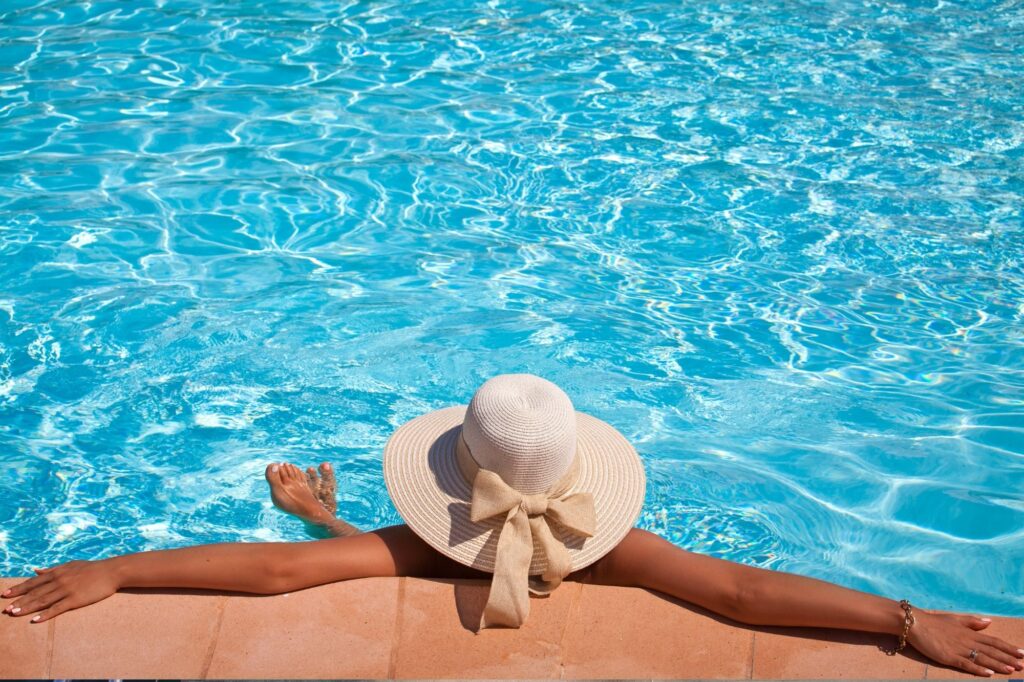 Poolside relaxation: person with a wide-brim straw hat resting their arms on the edge of a blue swimming pool.