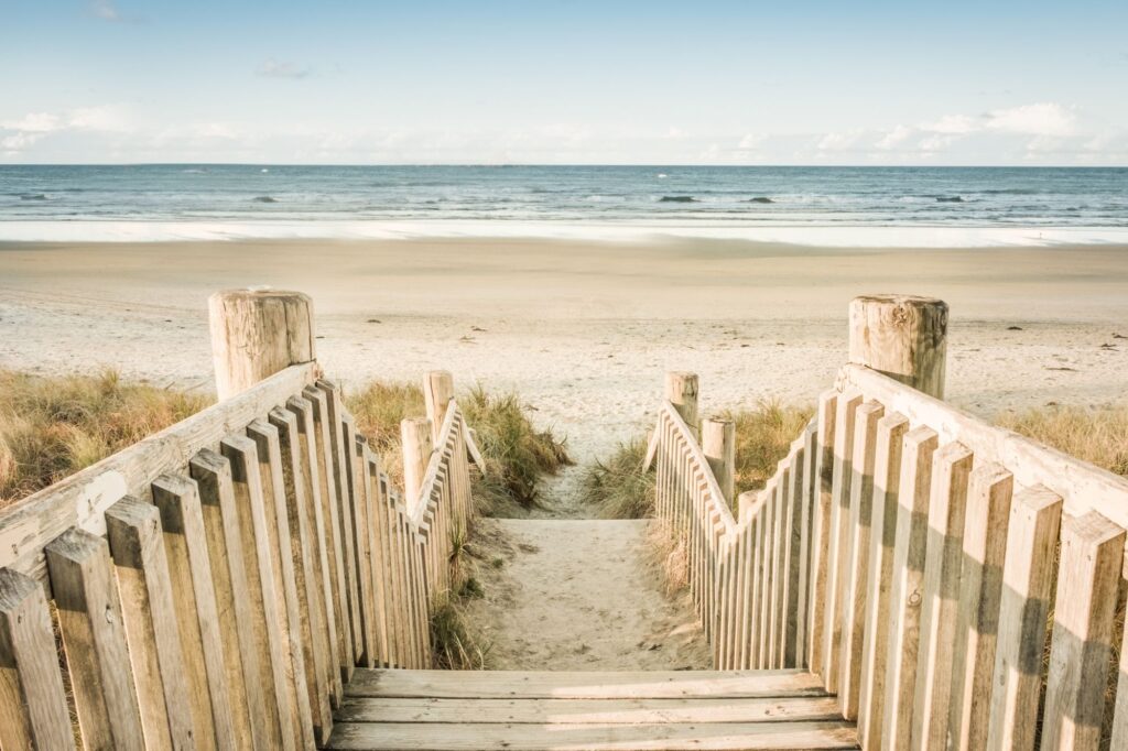 Wooden beach boardwalk leading to a sandy shore and blue ocean under a clear sky.