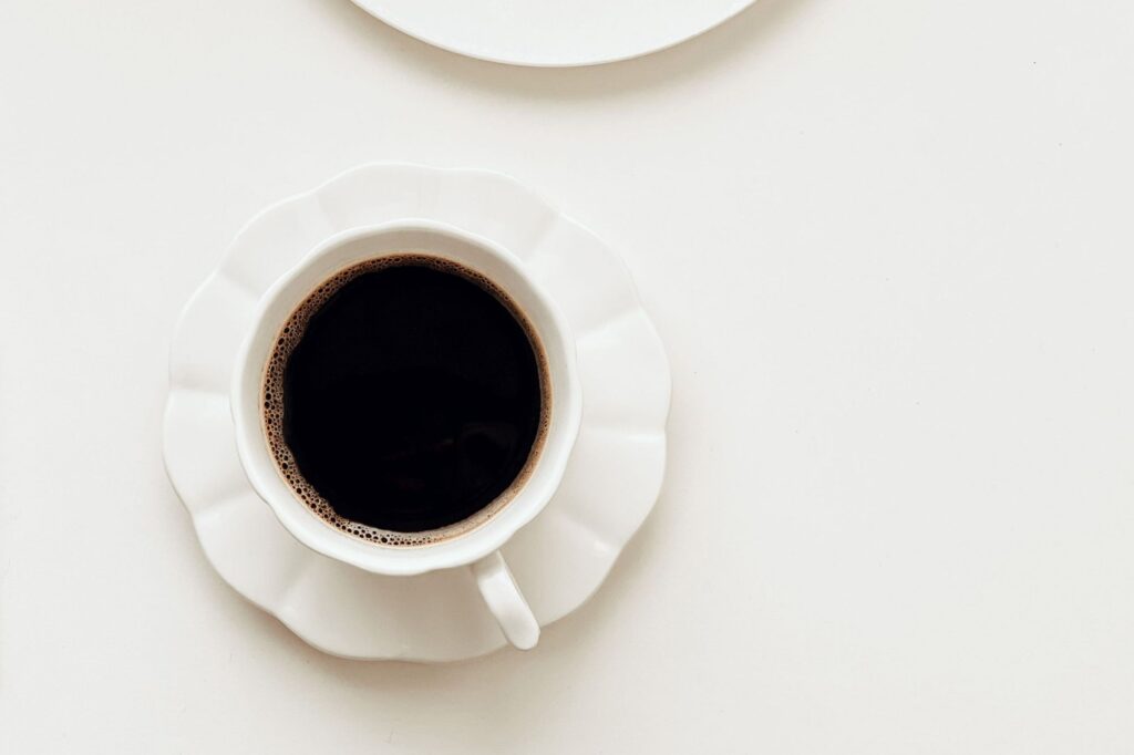 Top-down view of a white coffee cup filled with black coffee on a white saucer.