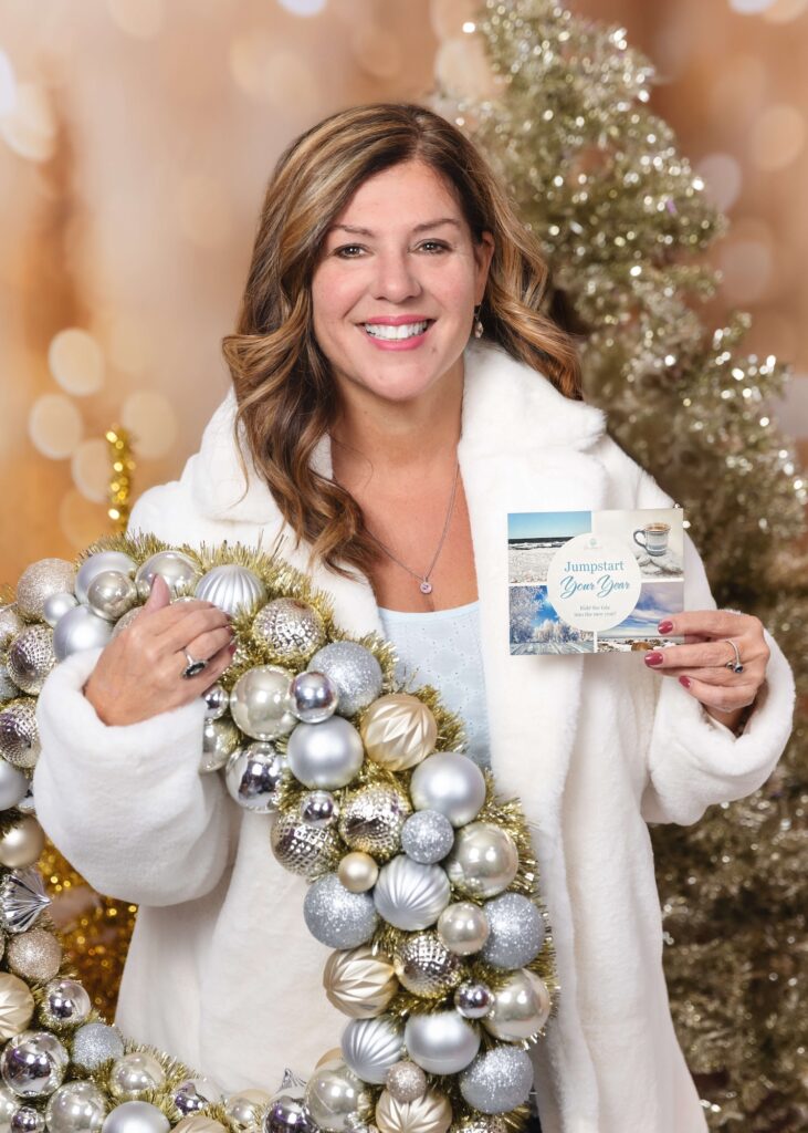 Smiling woman in a white coat holds a silver ornament garland and a holiday card.